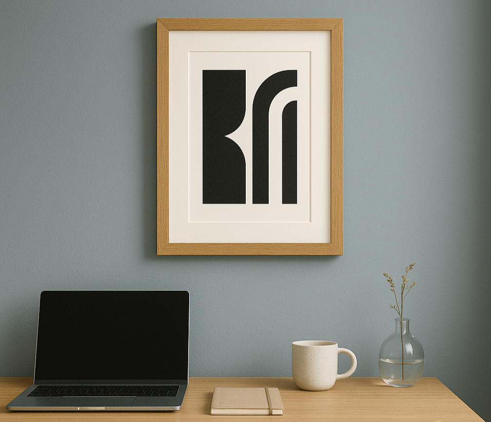 A3 premium oak frame with matboard showcasing bold black-and-white abstract artwork, hanging above a light timber desk in a home office with dusty blue walls and natural decor.
